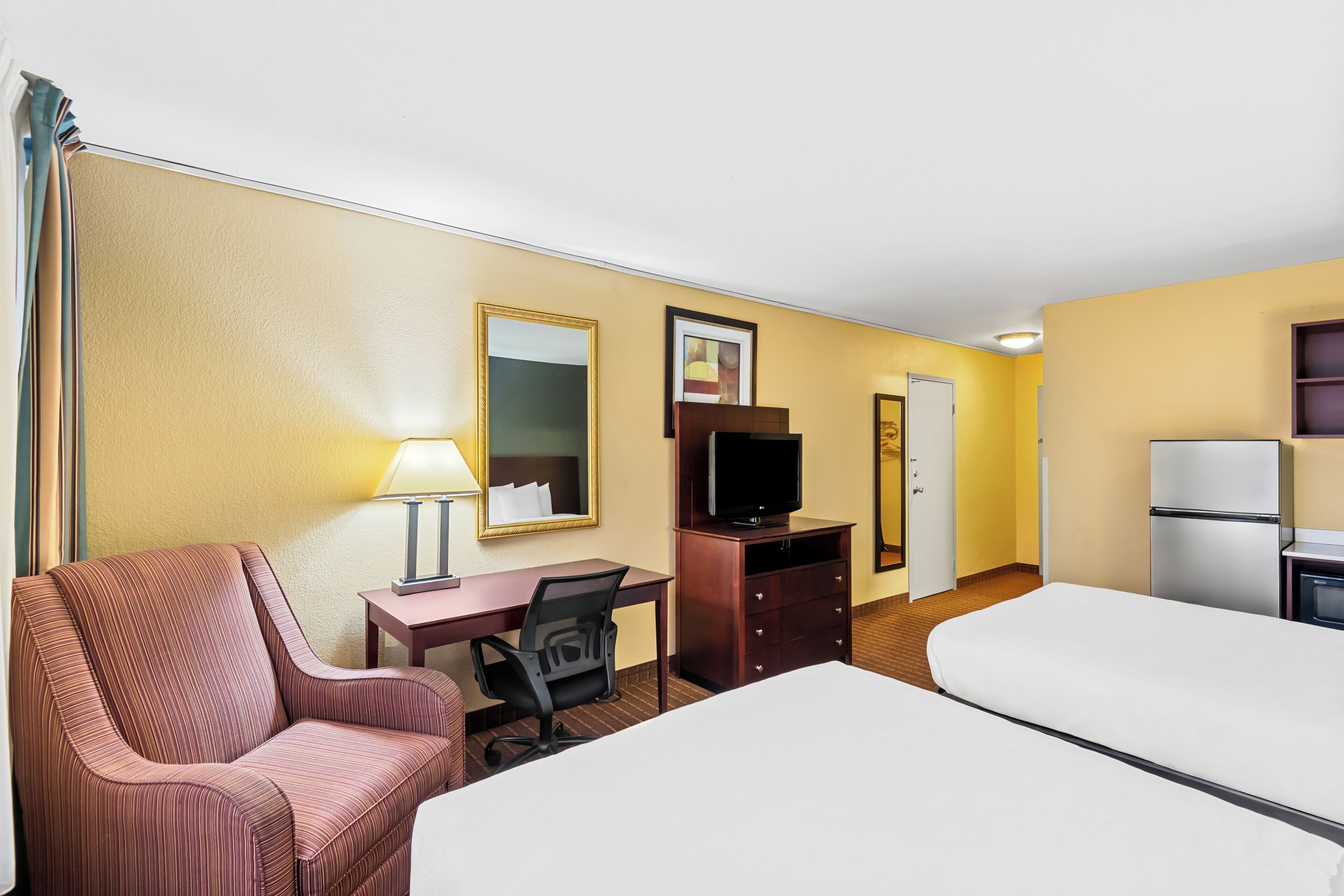 A hotel room with a bed, a desk with a chair, a television, a dresser, and a mirror.