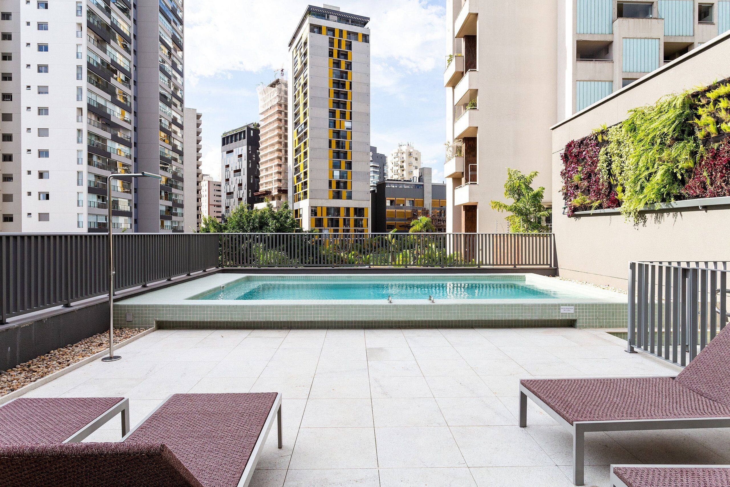 A rooftop pool area with lounge chairs, a tiled floor, and a view of surrounding high-rise buildings.