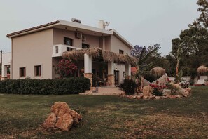 A modern two-story house with a covered porch, stone pillars, and a landscaped garden with various plants and rocks.