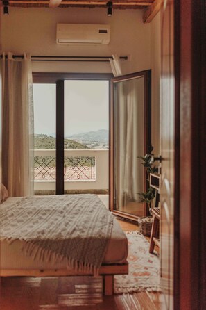 A bedroom with a bed, a balcony with a view, and an air conditioning unit.