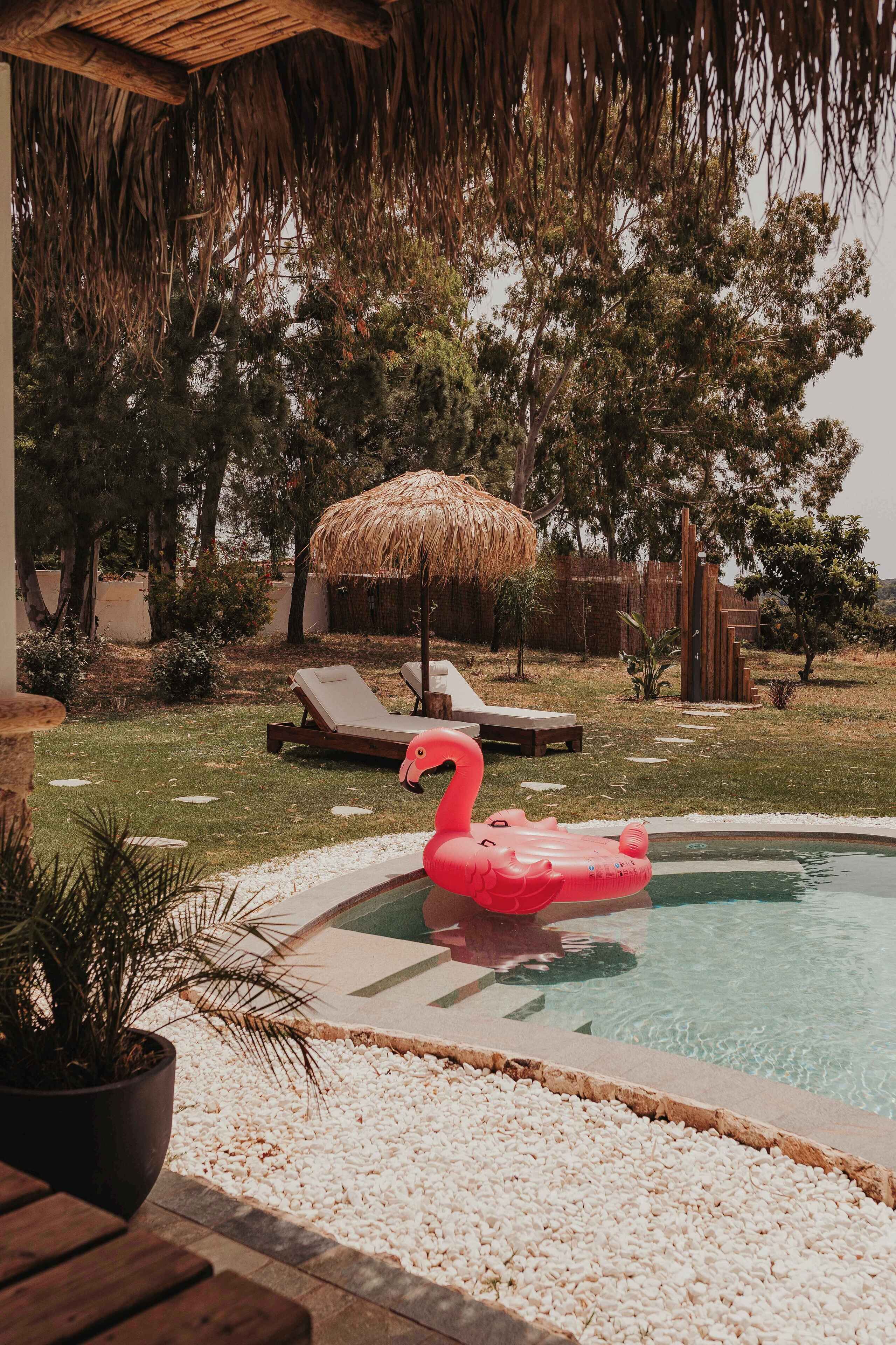 Et poolområde med en flamingo-svømmebøje, liggestole og en parasol af strå.