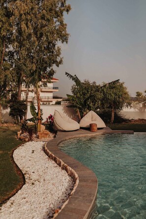A poolside area with a curved stone edge, white pebbles, and a few lounge chairs.