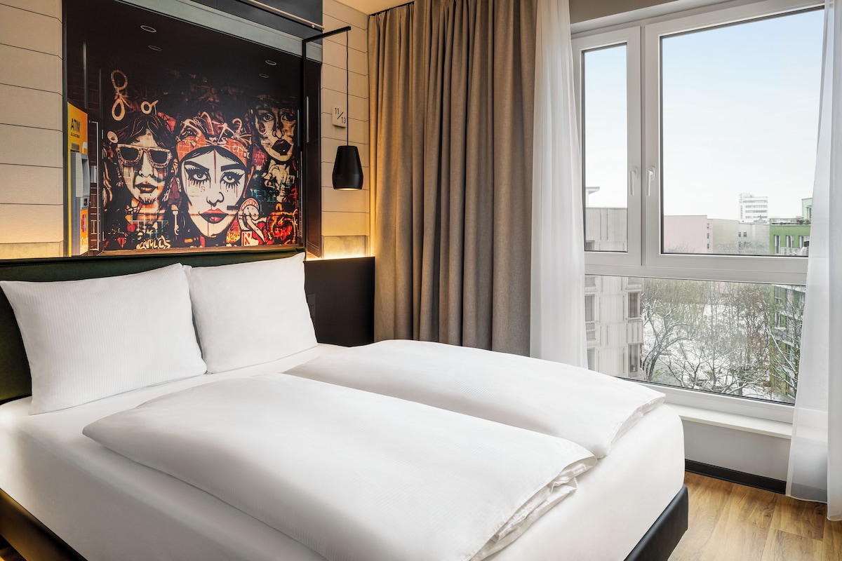 Habitación de hotel con una cama grande, vista a la ciudad y un mural en la pared.