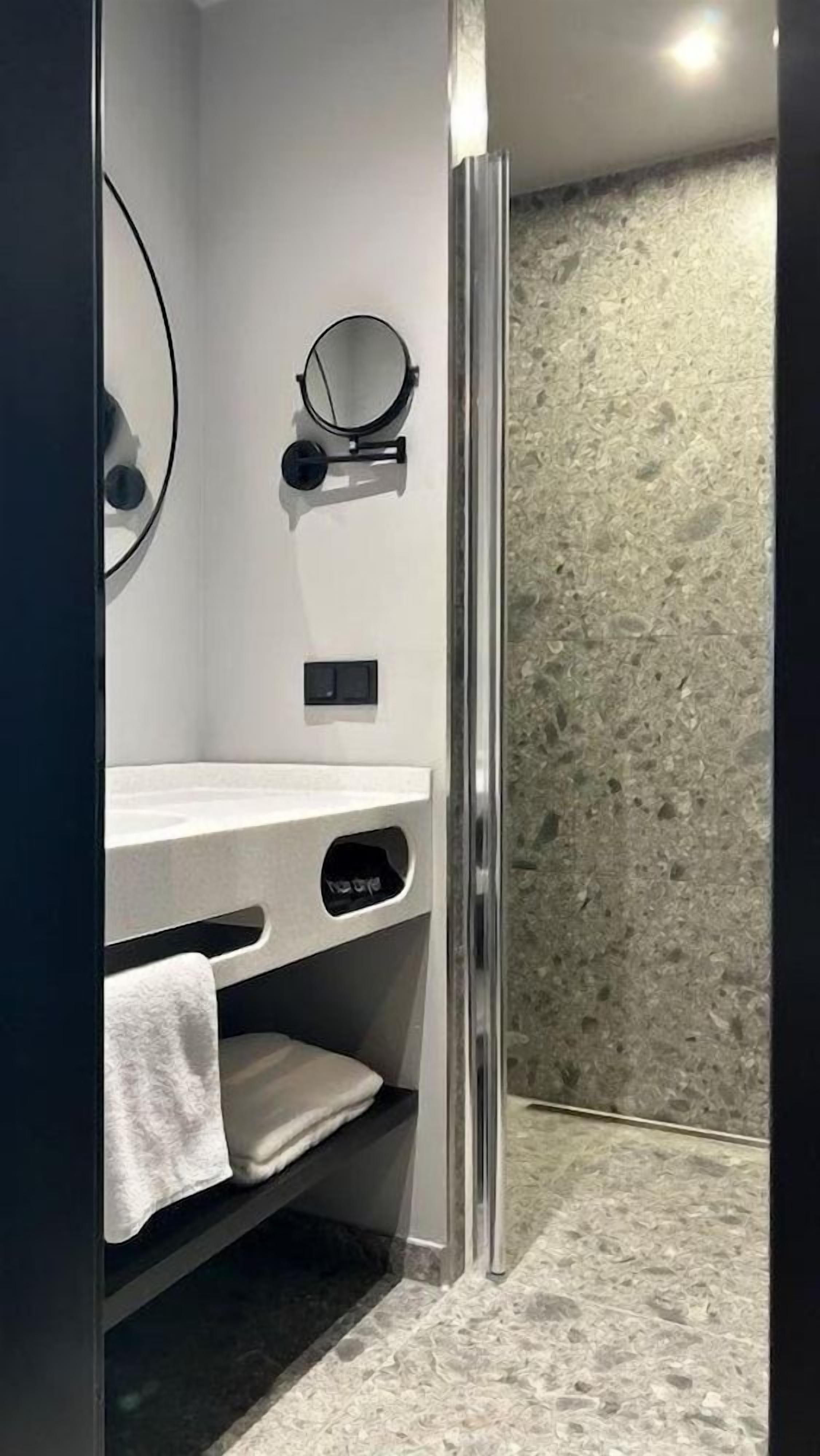 Un baño moderno con cabina de ducha de vidrio, tocador blanco con espejo y toallero.