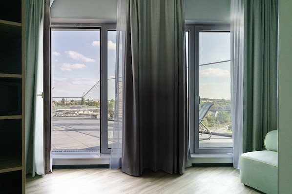 A room with a large sliding glass door leading to an outdoor area, a green sofa, and a view of a bridge and buildings. - Vienna House Easy Wyndham Berlin Potsdamer Platz (Berlin)