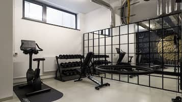 Ein Fitnessraum mit Trainingsgeräten, einem Fenster und Lüftungsrohren an der Decke.