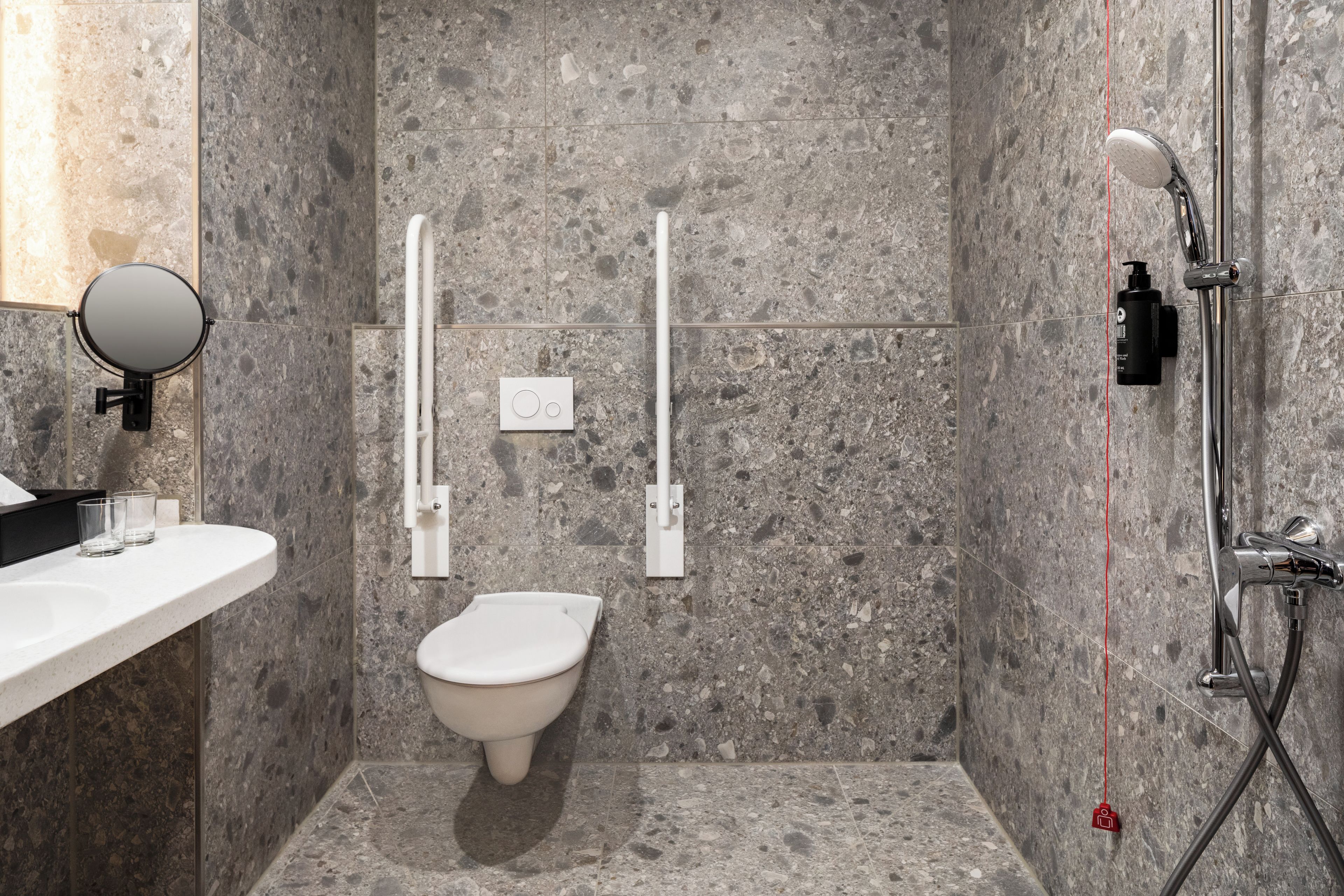 Ein modernes Badezimmer mit Marmorboden, Toilette in Weiß, Waschbecken mit Spiegel und Dusche mit Handbrause.