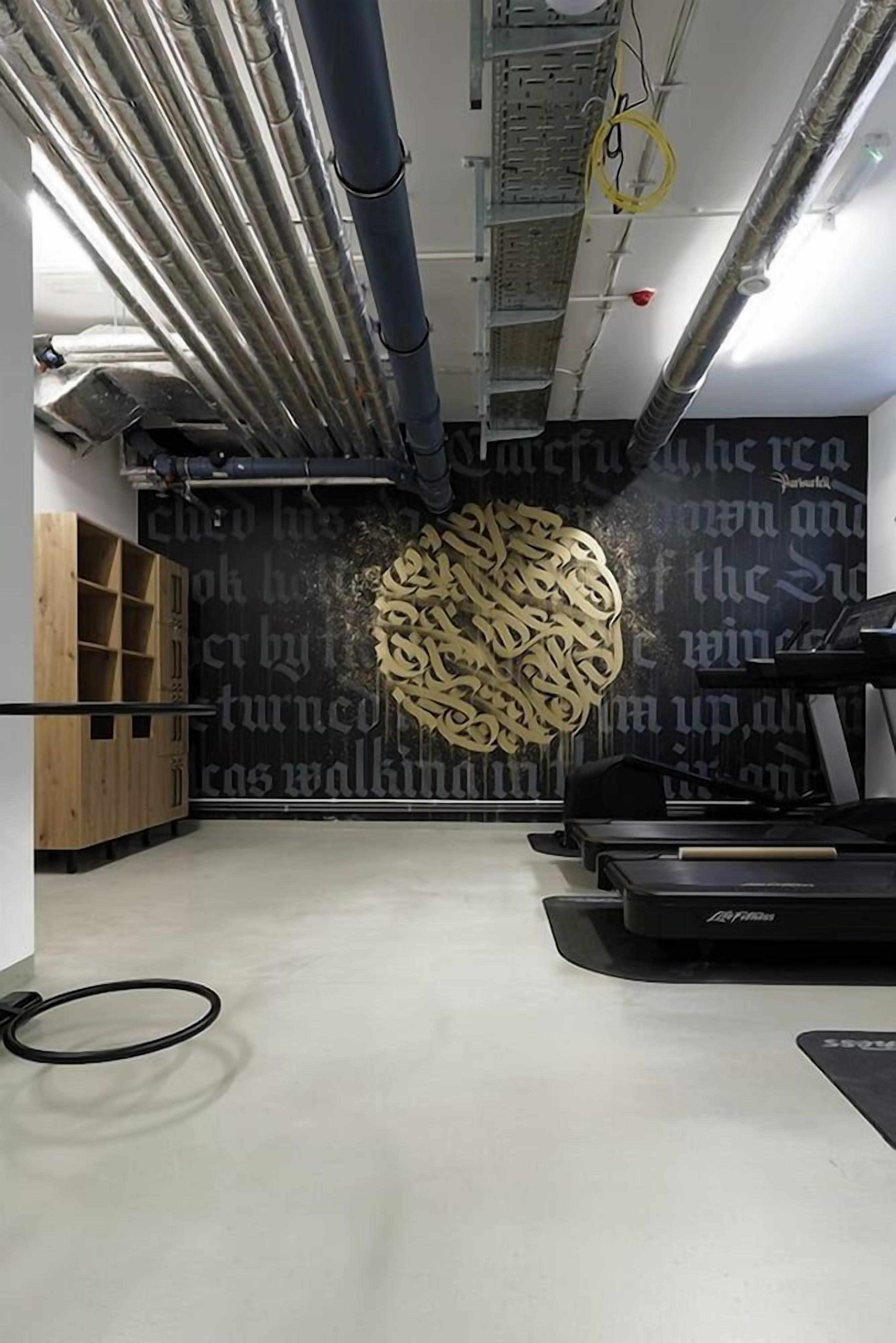 A gym with exercise equipment, a large decorative wall, and visible ductwork.