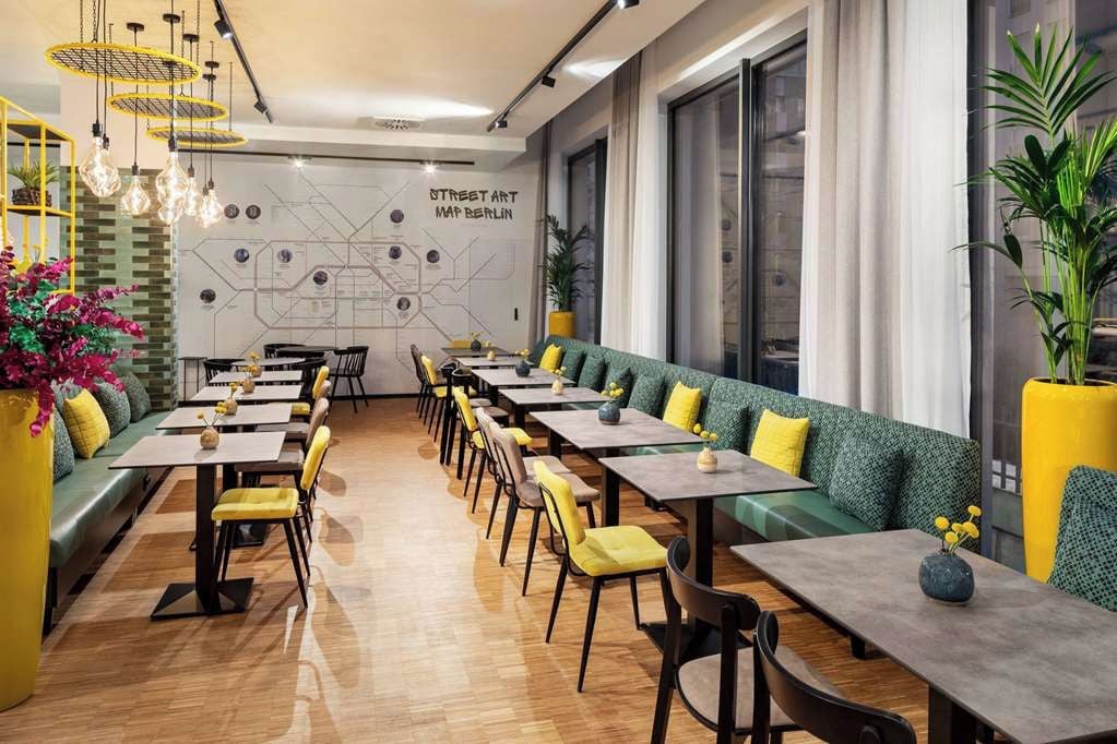 Un restaurante moderno con mesas largas comunitarias, asientos tapizados en verde e iluminación decorativa.