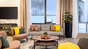 A modern living room with a patterned sofa, a flat-screen TV, and a large window with a view of the cityscape. - Vienna House Easy by Wyndham Berlin Potsdamer Platz (Berlin)