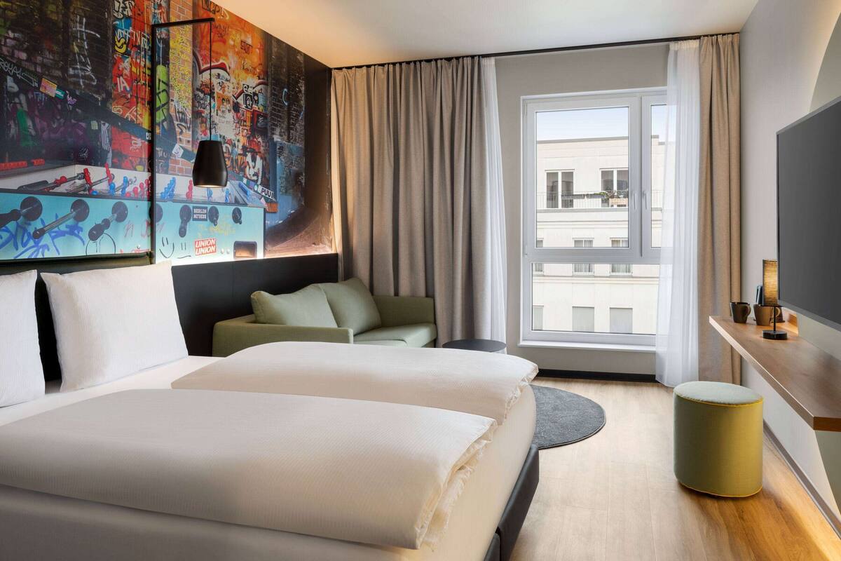 A hotel room with a large bed, a sofa, a small table, a TV, and a window with curtains.