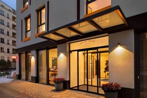 A modern hotel entrance with a glass facade, outdoor seating, and a sign reading 'VIENNA HOUSE.'