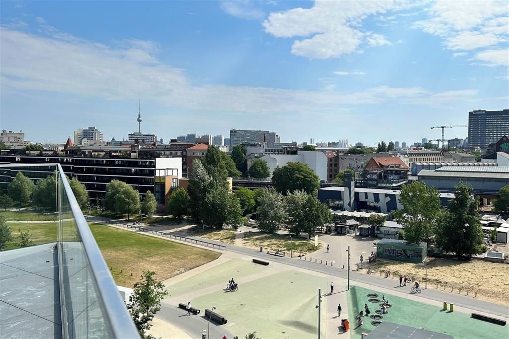 Un paysage urbain avec des bâtiments modernes, une tour imposante et un espace vert doté de sentiers et de bancs.
