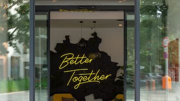 Der Eingang des Vienna House by Wyndham, mit modernem Design, einer Glastür, einem roten Teppich und dem Schriftzug "Better Together" an der Wand.