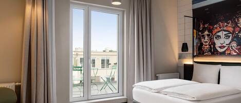 A hotel room with a large window, a bed, a chair, and a painting on the wall.