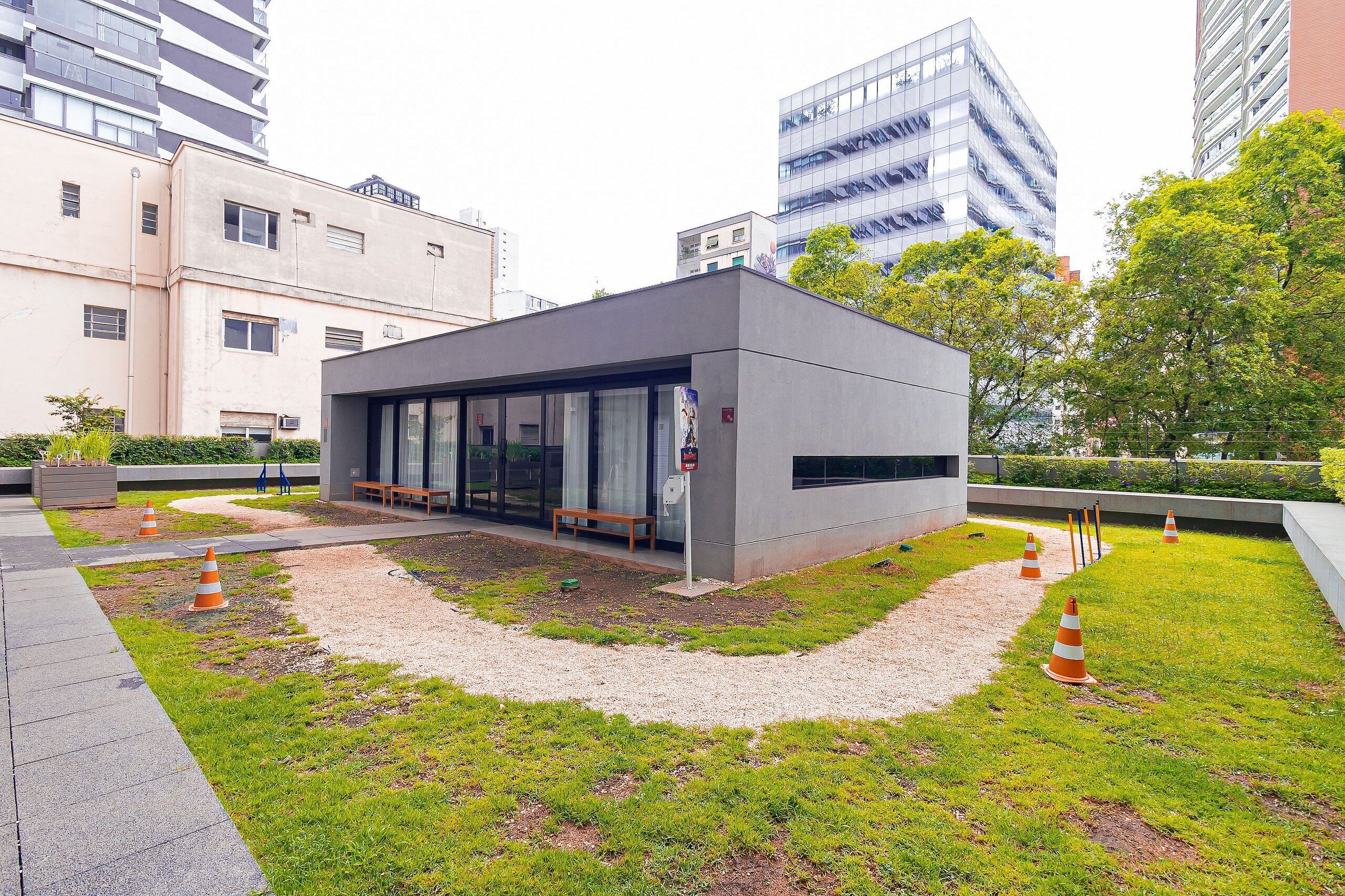 A modern building with a flat roof, large windows, and a small garden area with a pathway and orange traffic cones.