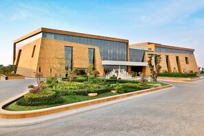 A modern building with a large glass facade, a landscaped garden with various plants and a water feature, and a paved entrance area.