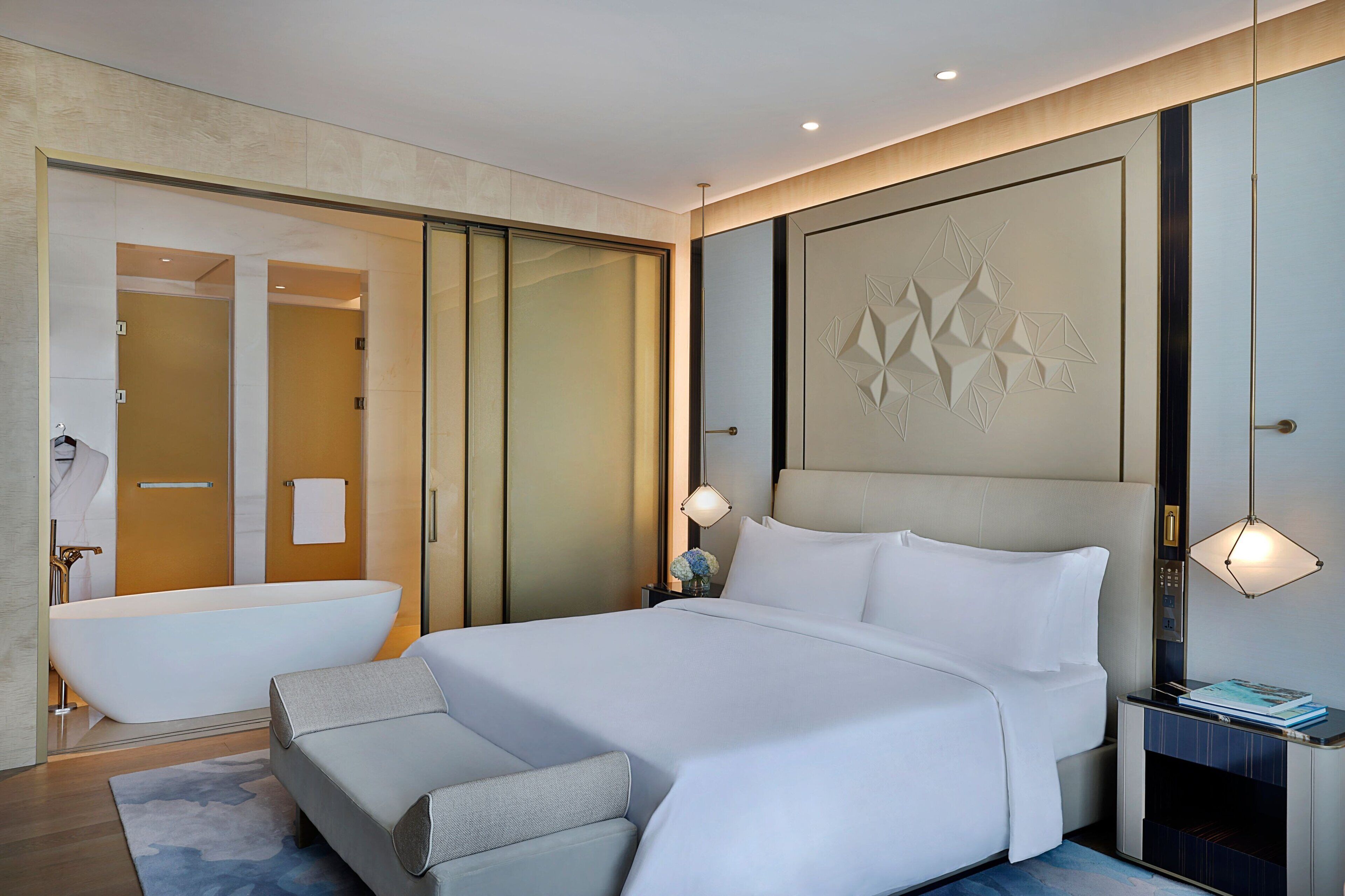 Habitación de hotel moderna con una cama grande, un baño independiente con bañera y una mesita de noche con lámpara.