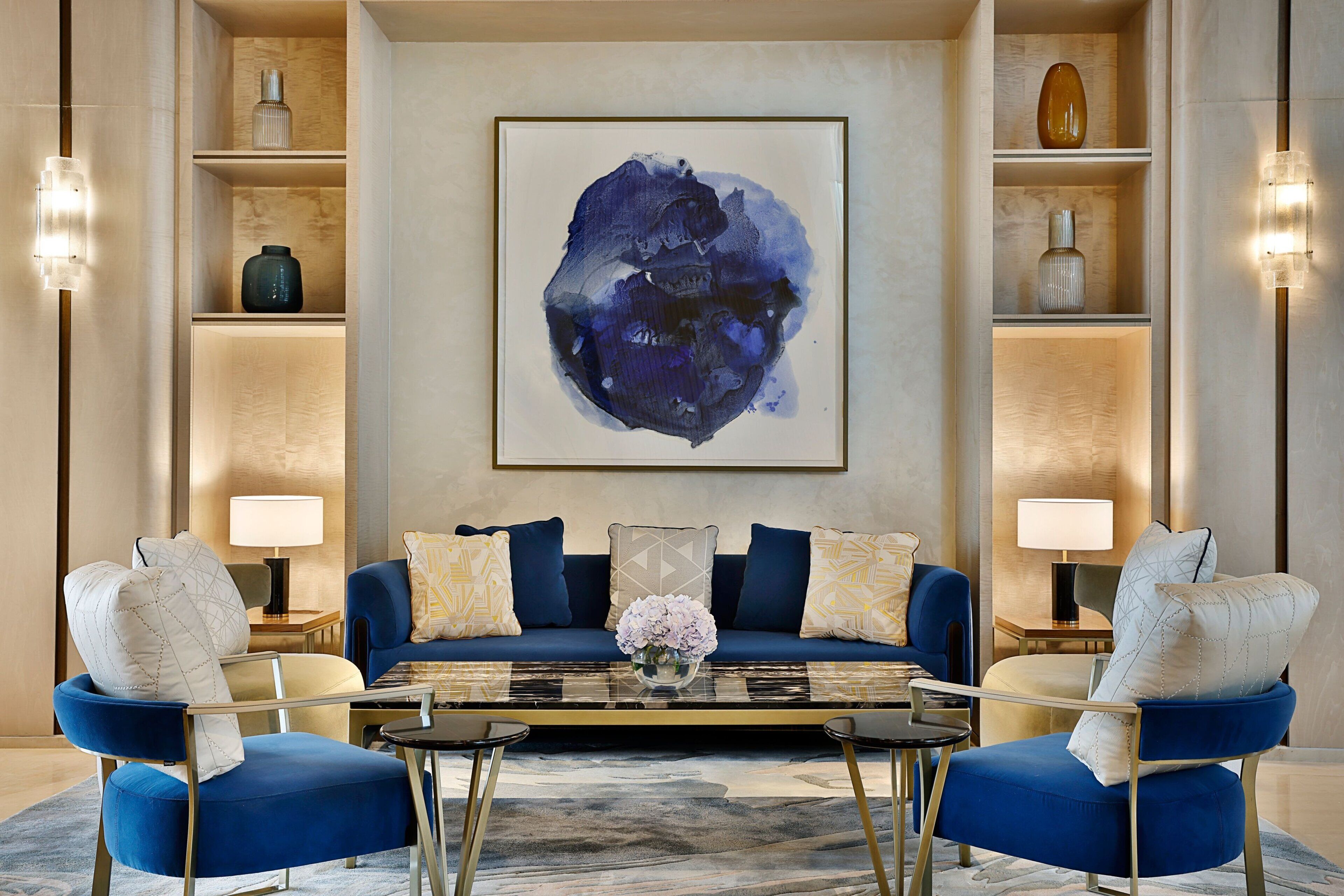 Una sala de estar moderna con un sofá azul, dos sillones, una mesa de centro y un cuadro abstracto grande en la pared.