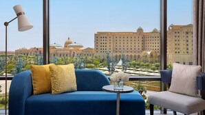 A room with a large window offering a view of a grand building with domes and a fountain. There is a blue sofa with a yellow pillow and a white chair with a patterned pillow.
