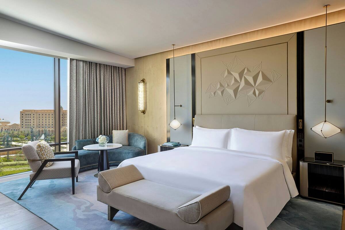 A modern hotel room with a large bed, a sofa, a small table, and a view of the cityscape.