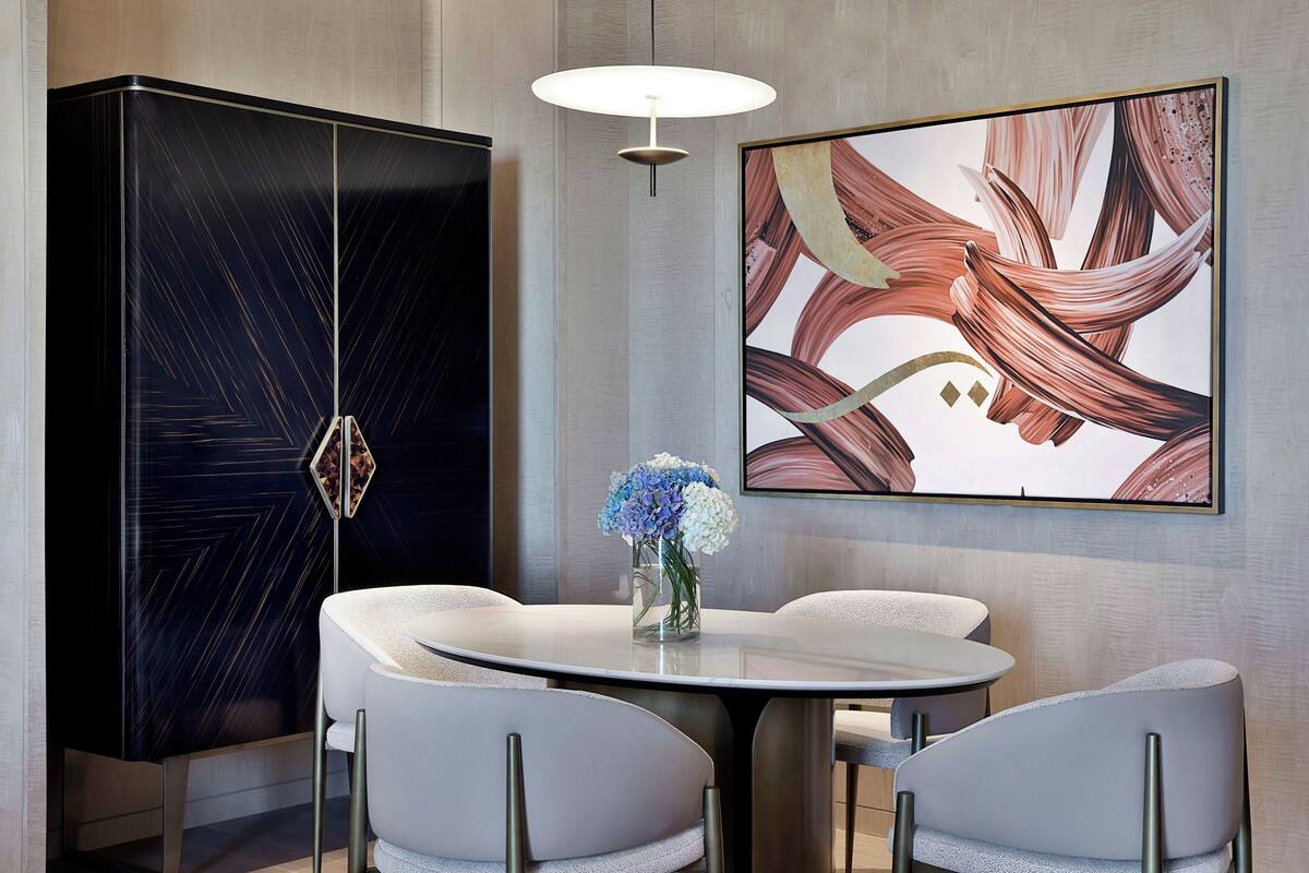 A modern dining area with a round table and four chairs, a black cabinet, and a large abstract painting on the wall.