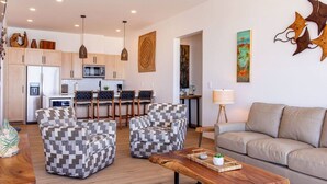 A modern living room with a sofa, two patterned armchairs, a wooden coffee table, and a kitchen in the background.