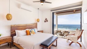 A bedroom with a large bed, wooden headboard, bench, and a view of the ocean.