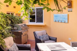 Una veranda esterna con mobili in vimini, un barbecue e un cartello con le regole della casa sulla spiaggia.