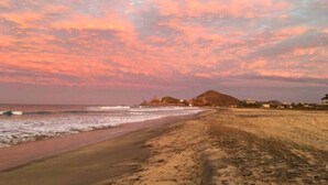 Una playa con un atardecer, olas y edificios a lo lejos.