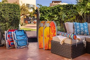 Un'area patio con un divano in vimini, cuscini colorati e due tavole da surf.