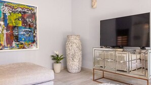 Una sala de estar moderna con un cuadro abstracto grande, un jarrón alto y texturizado, un mueble de televisión con espejo y un sofá mullido.