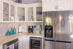 Une cuisine avec des meubles blancs, un réfrigérateur en acier inoxydable, une machine à café et un distributeur d’eau.