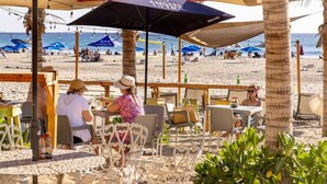 Un área de estar al aire libre con mesas, sillas, sombrillas y vistas a la playa.