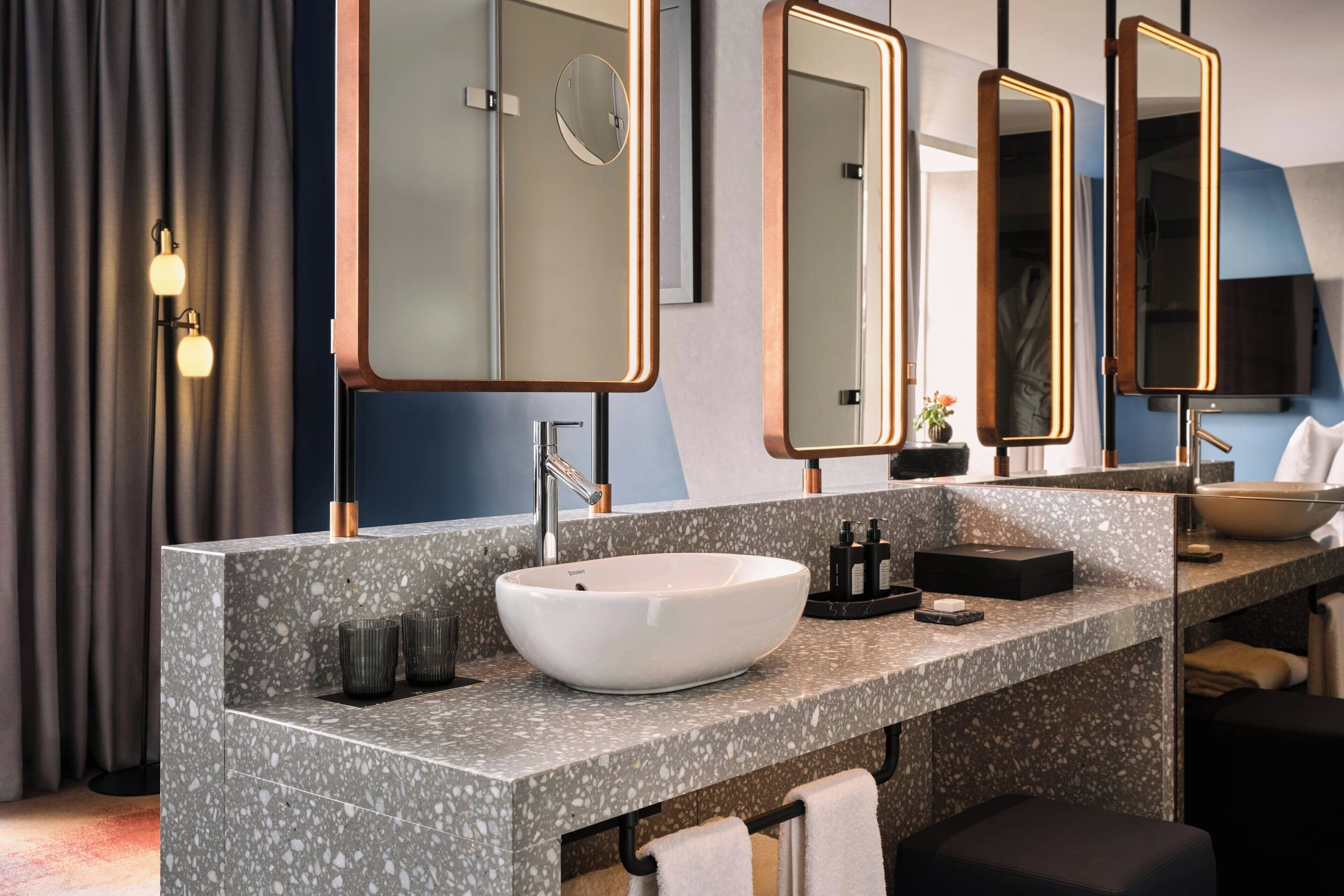 A modern bathroom with a large, round vessel sink, multiple mirrors, and a granite countertop.