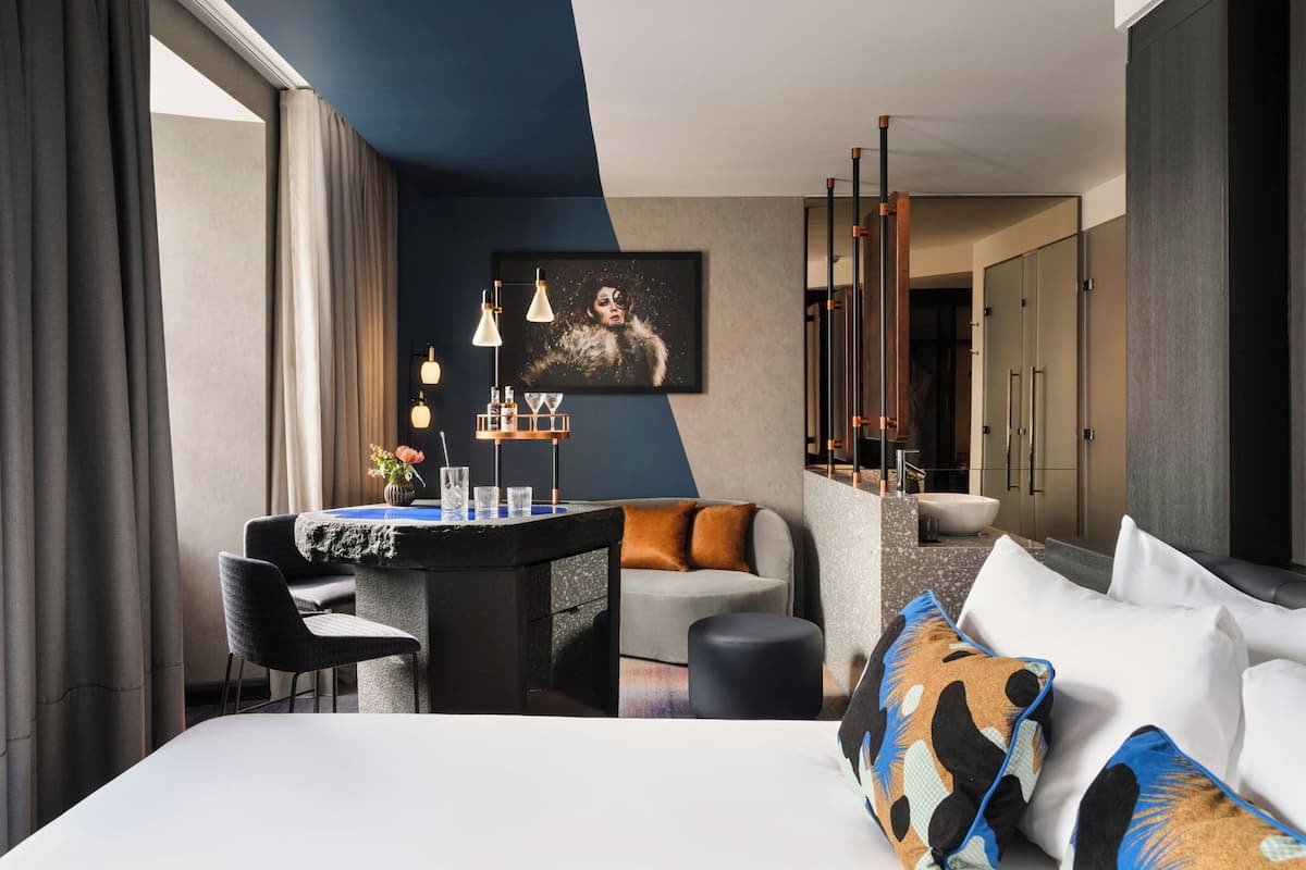 A modern hotel room with a large bed, a desk with a view, a sofa, and a painting on the wall.