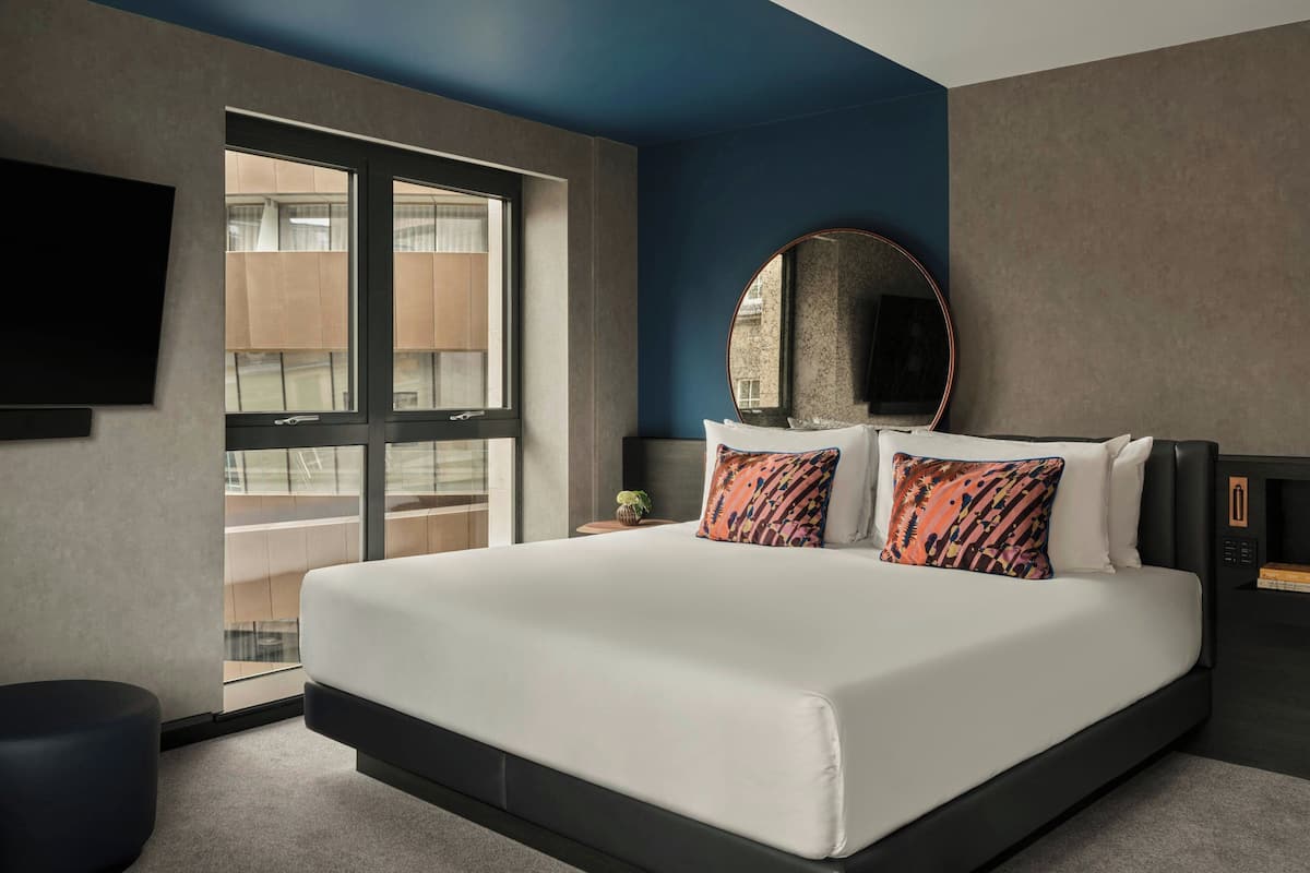 A modern hotel room with a large bed, a round mirror, and a TV mounted on the wall.