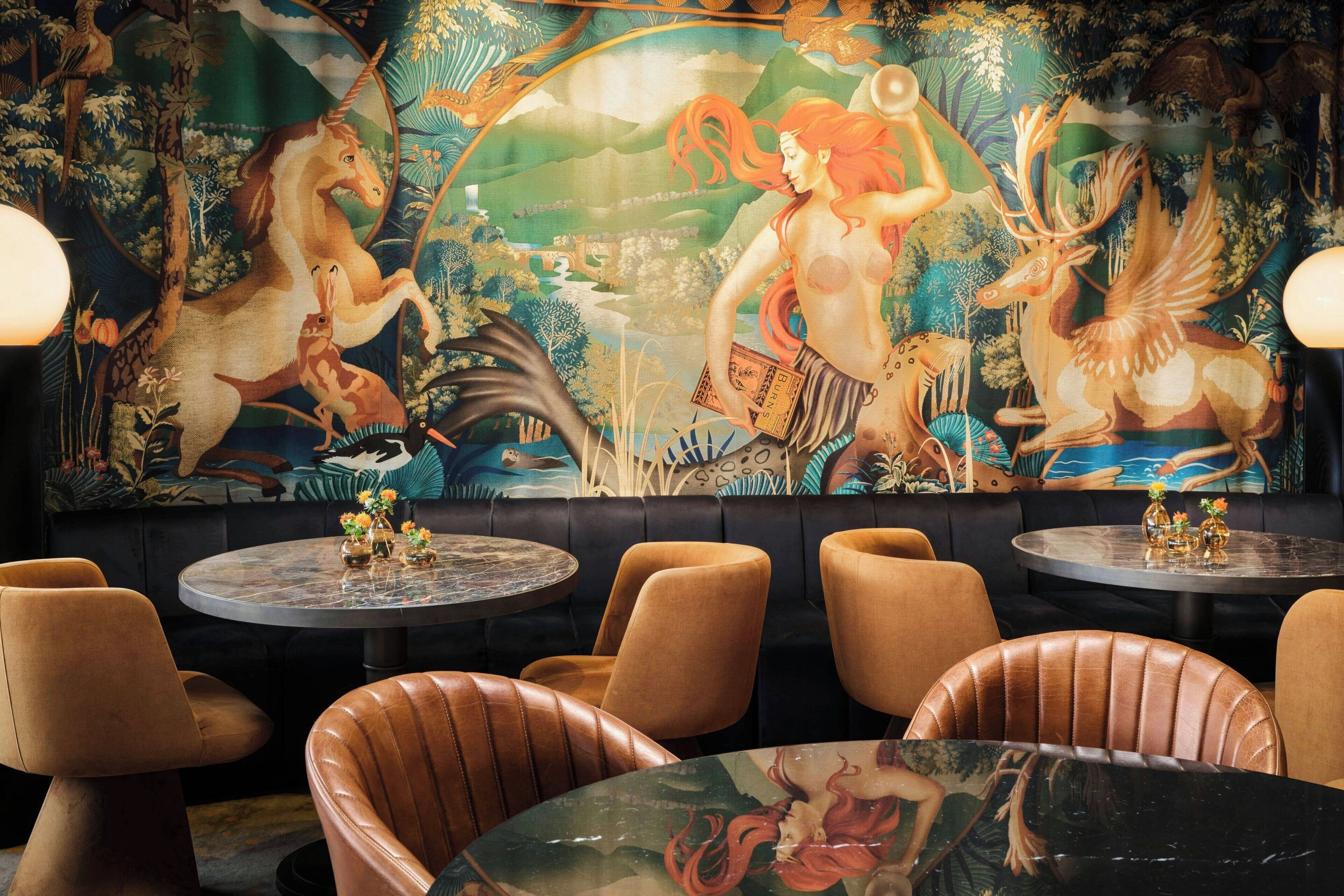A restaurant with round tables and leather chairs, featuring a mural with mythical creatures and a forest scene.
