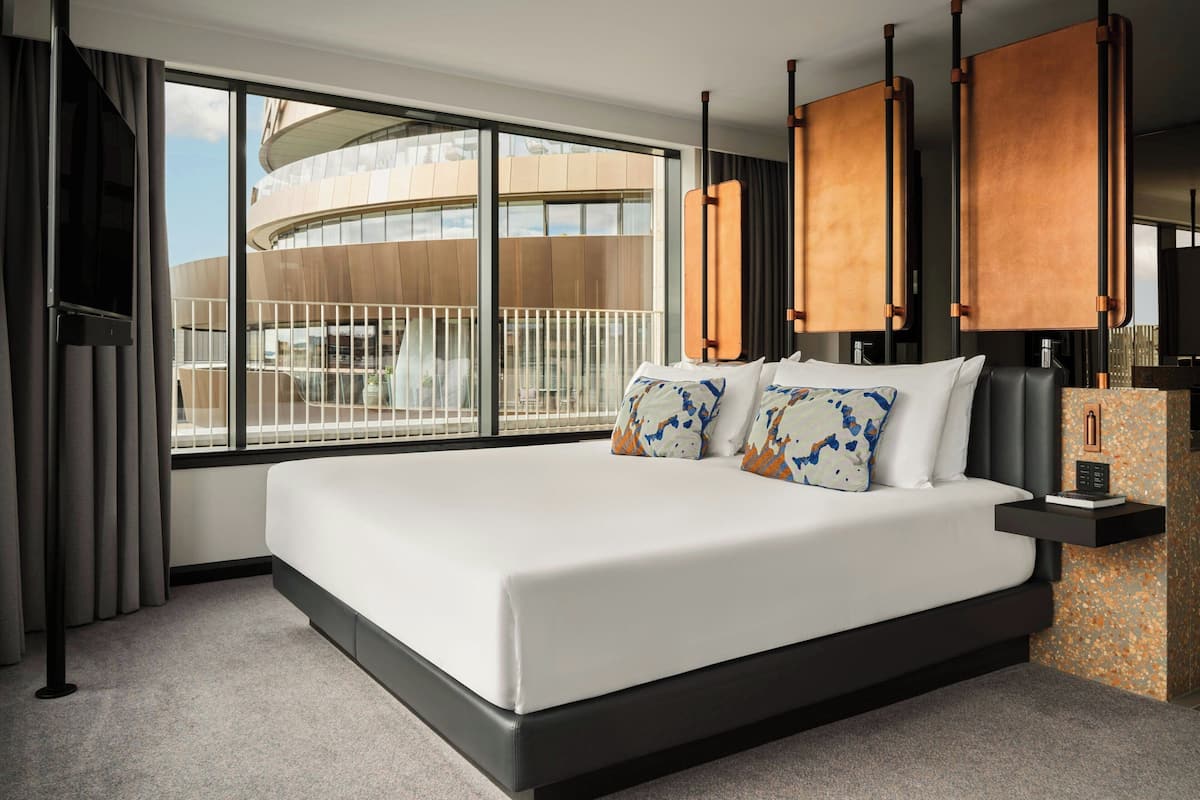 A modern hotel room with a large bed, a view of a building, and a balcony.
