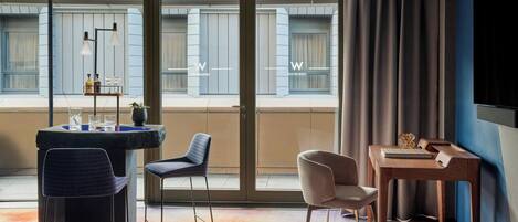 Una habitación de hotel moderna con un ventanal grande, un escritorio con computadora, una silla y una mesita con una botella y vasos.