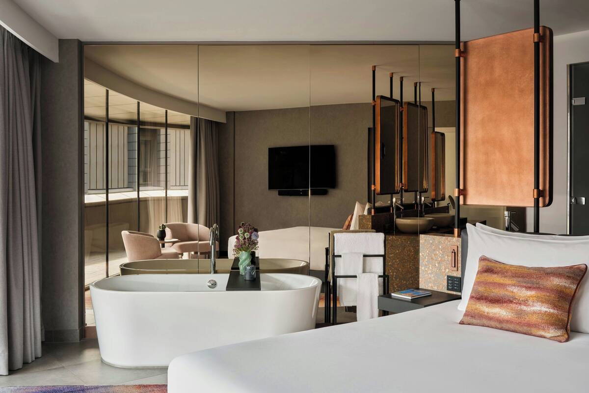 A modern hotel room with a large bed, a bathtub, a flat-screen TV, and a large window with curtains.