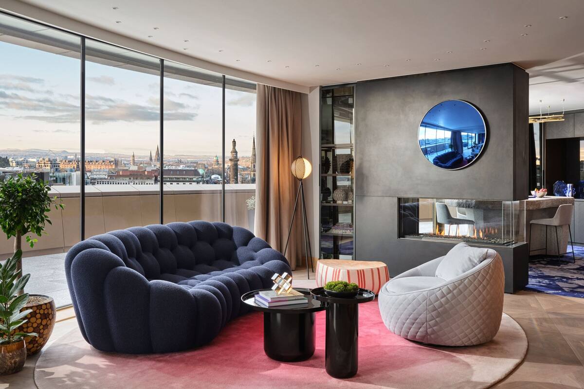A modern living room with a large window, a round mirror, a fireplace, and a city view.