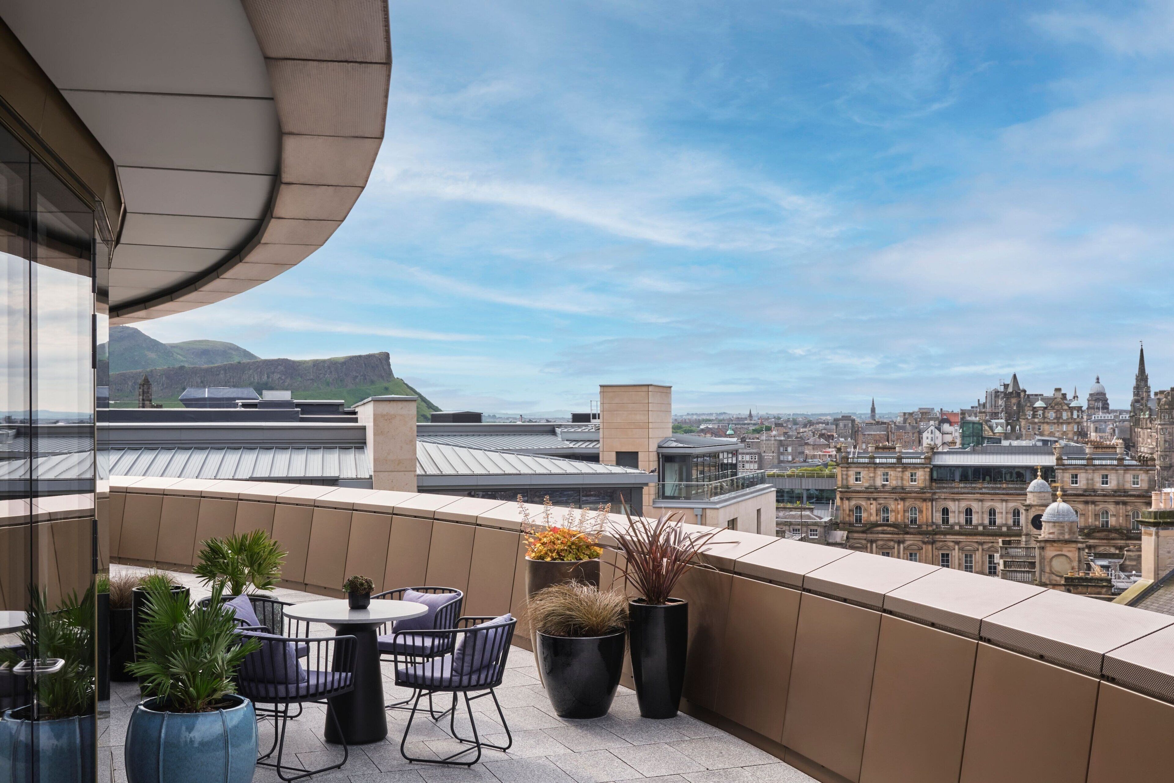 A balcony with a city view, featuring a table and chairs, potted plants, and a curved ceiling.