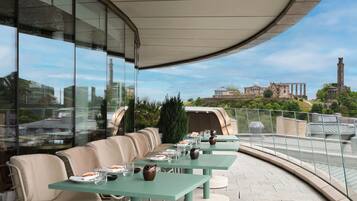 An outdoor dining area with tables and chairs, overlooking a historic building and a tower.