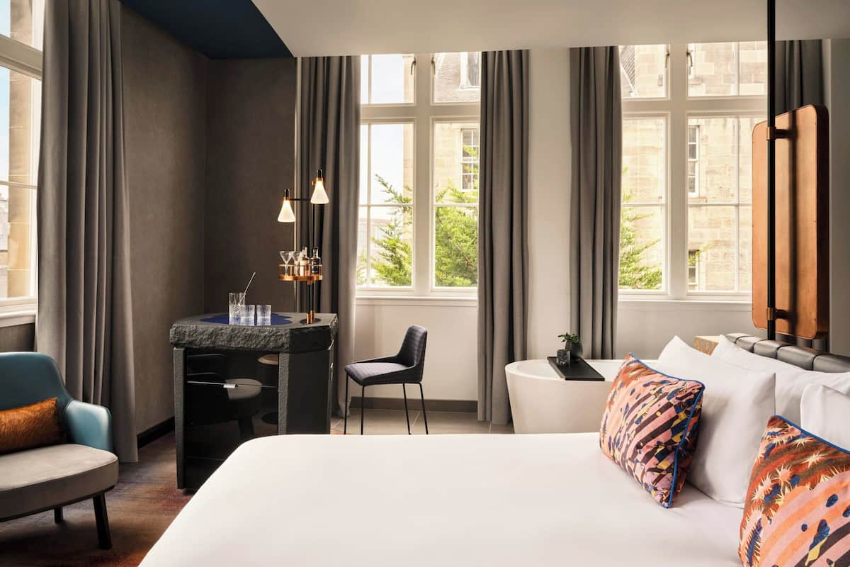 A hotel room with a bed, a desk, a chair, and a large window with curtains.