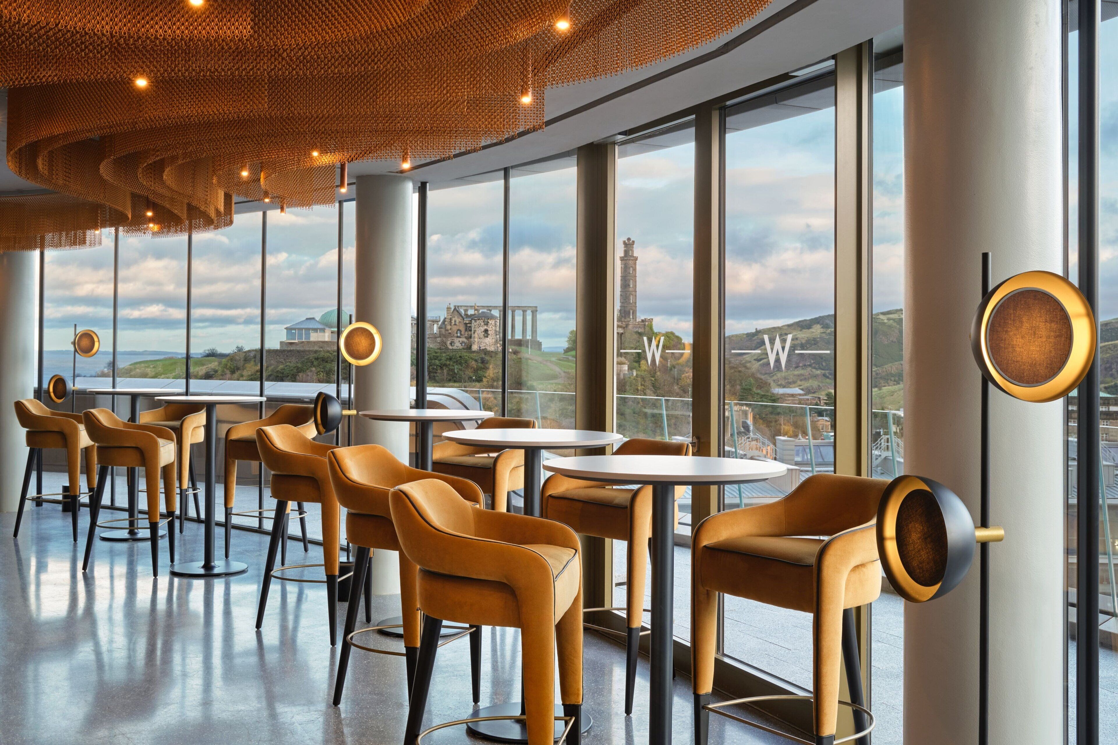 A modern interior with round tables and chairs, large windows with a view of a historic building, and a unique ceiling design.
