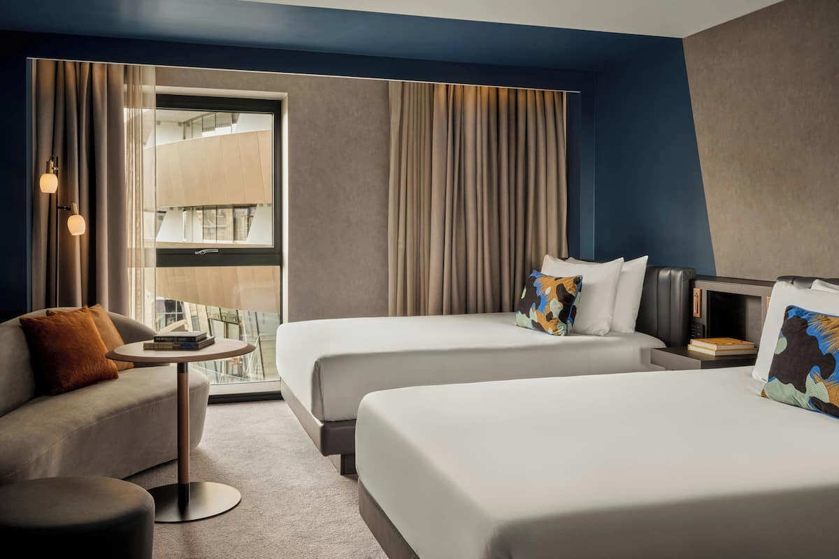 A hotel room with two beds, a sofa, a small table, and a window with curtains.