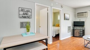 A modern living room with a wooden floor, a dining table, a TV, and a bed with a yellow pillow. - Lakefront Oasis: Boat Slip, Kayaks & Outdoor Pool (Kimberling City)
