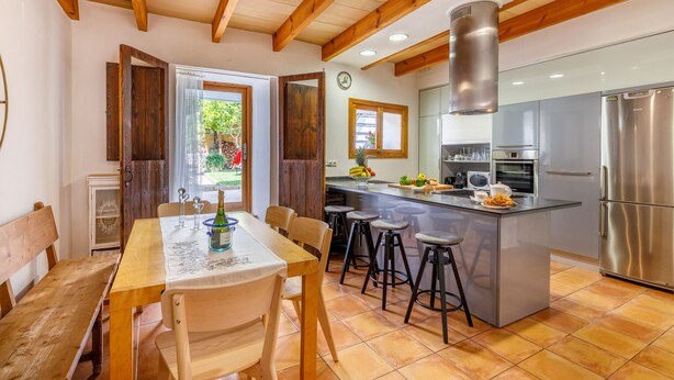 A kitchen with a wooden table, stools, and a stainless steel refrigerator.