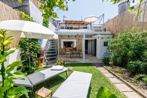 Un patio trasero con zona de estar, una silla de descanso, una mesa y un pequeño jardín.